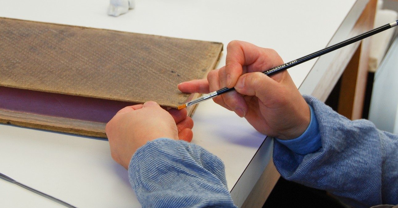 Conservator consolidates delaminating book cover edge