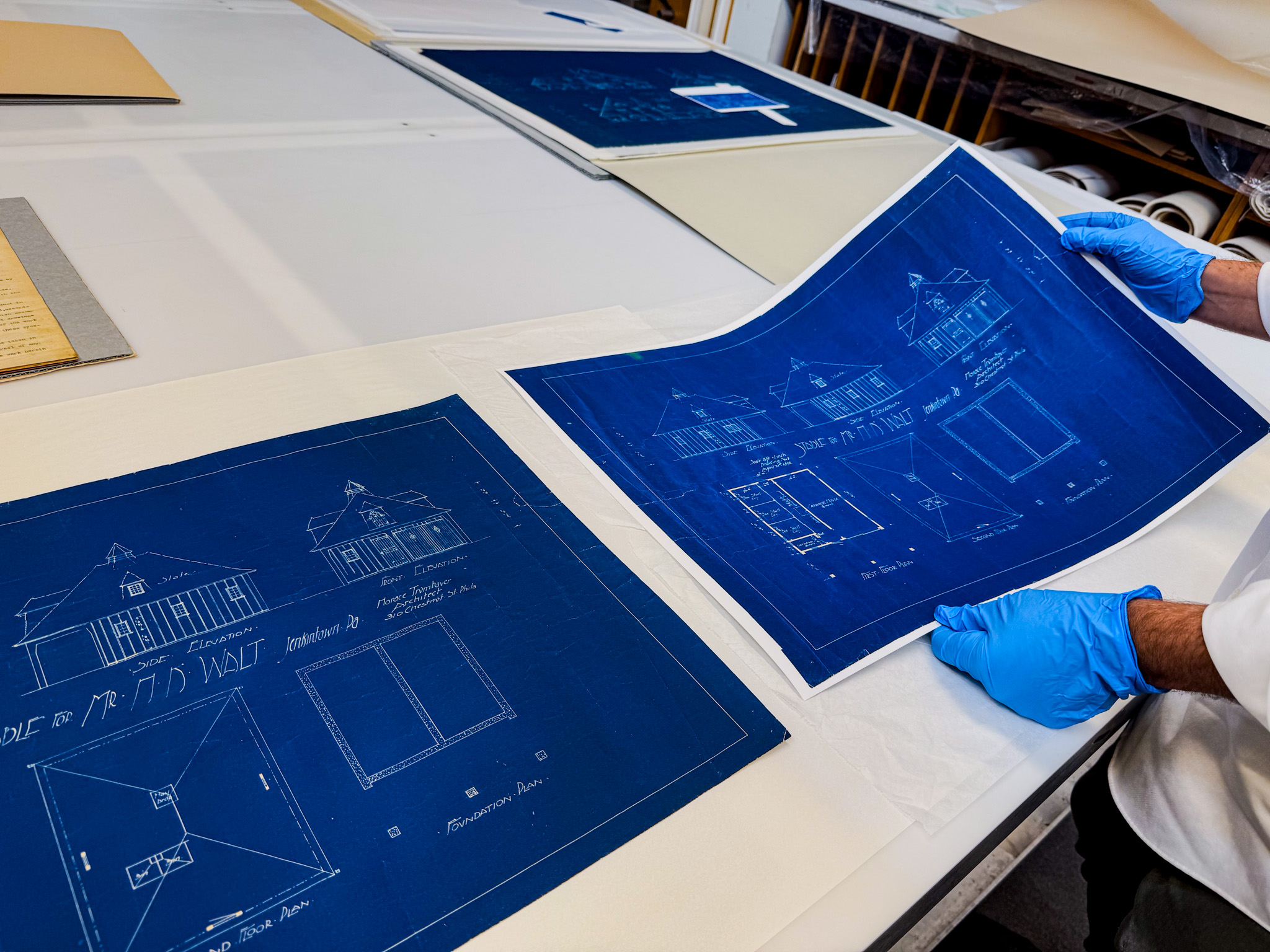 An individual wearing gloves holds architectural blueprints